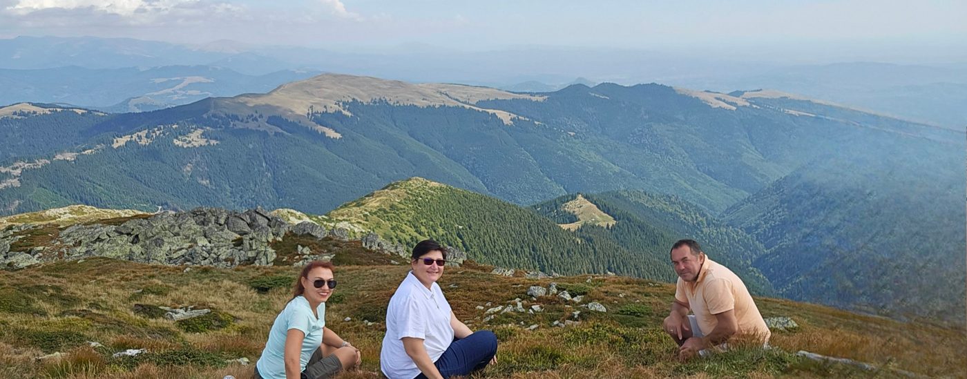 Guests resting on the grassy summit of Leaota, with forested ridges behind