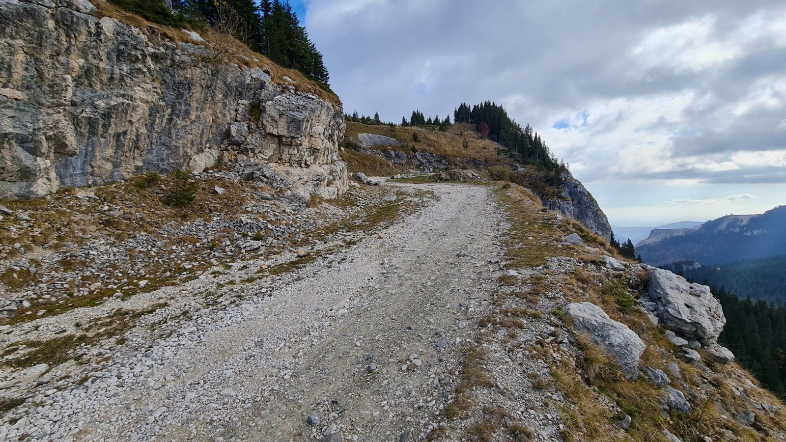 Gravel trail along a limestone cliff above forested valleys in the Bucegi Mountains