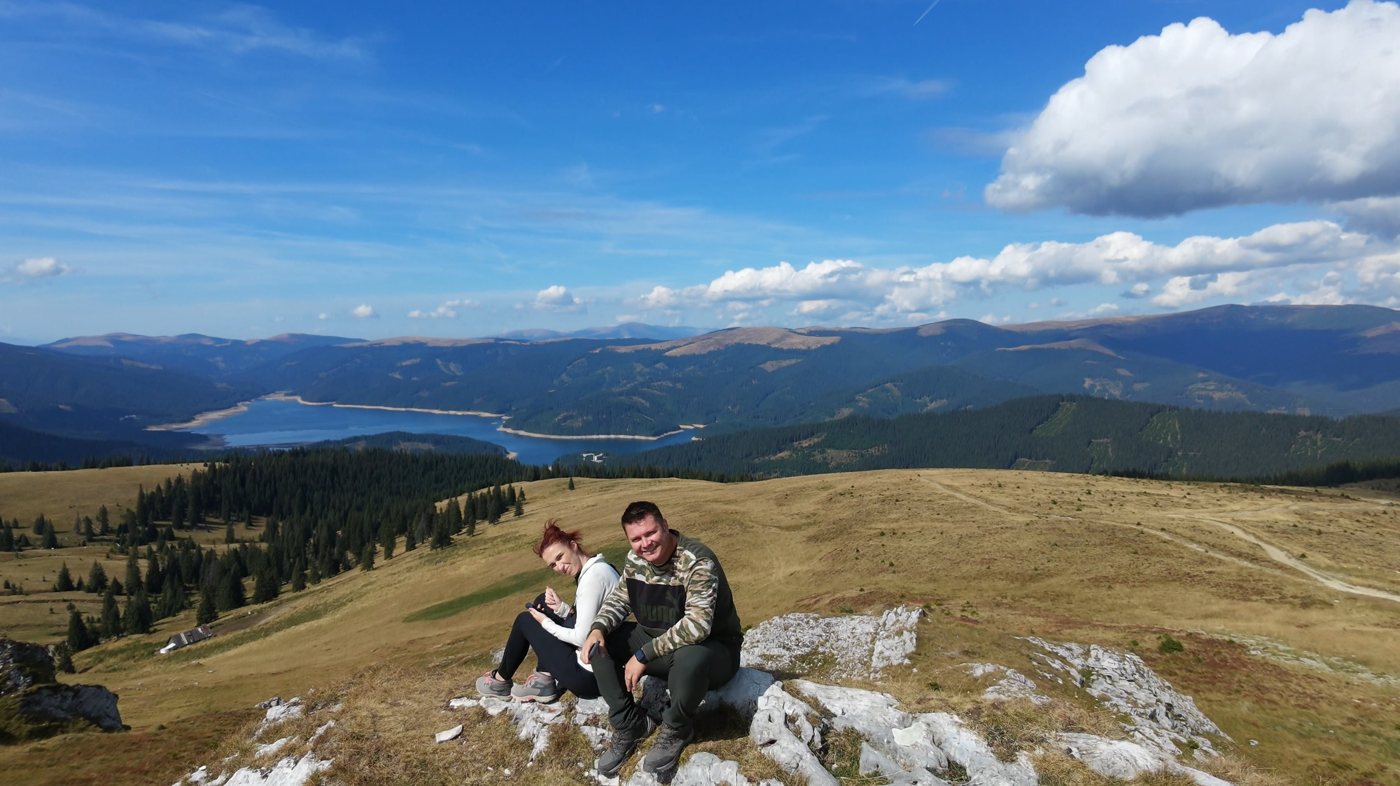 Nicoleta and Alex sitting on a rock on the Strategica ridge, with Lake Vidra and the mountains behind them