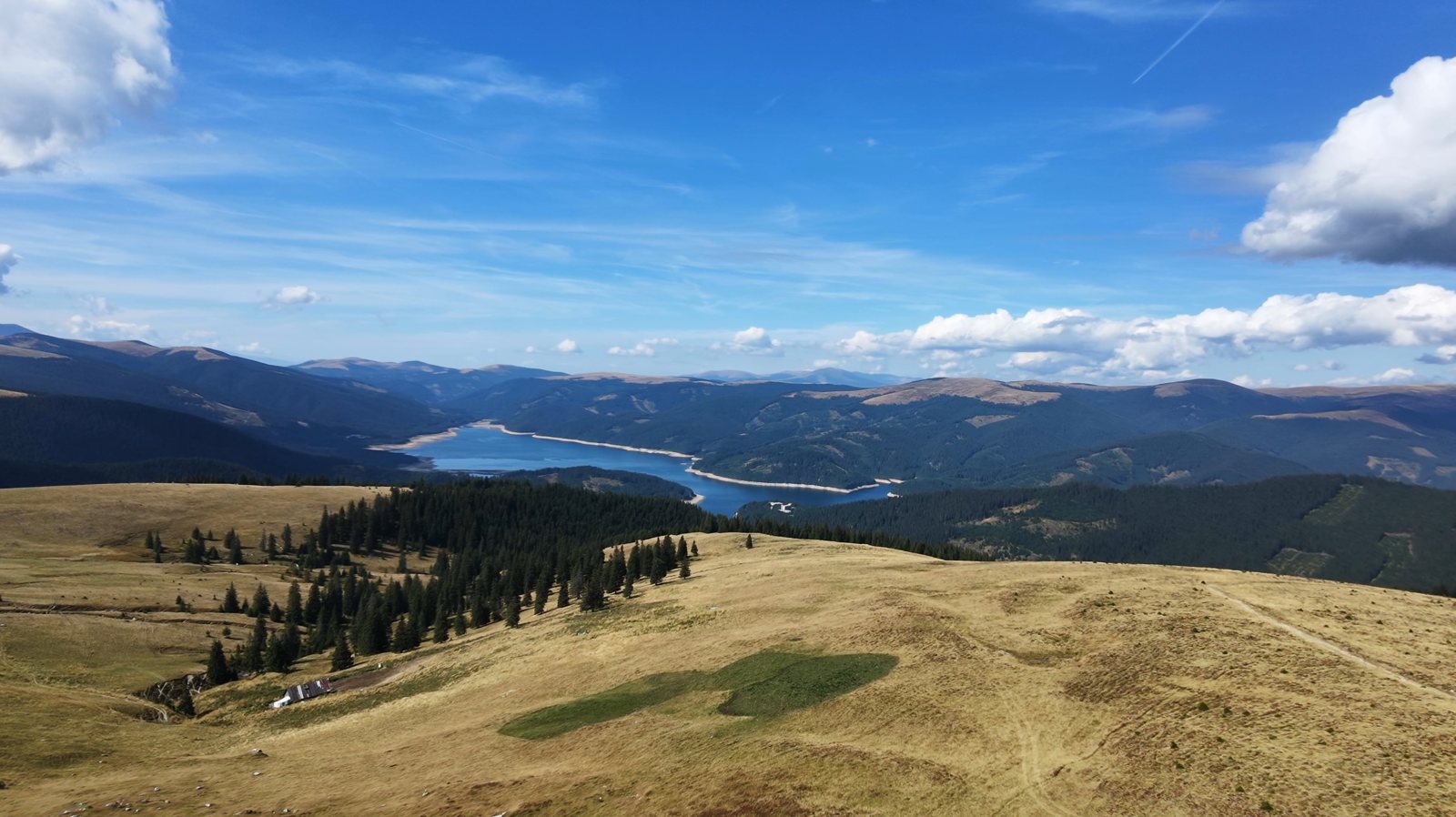 Drone view over golden alpine meadows towards Lake Vidra, seen from the Strategica ridge