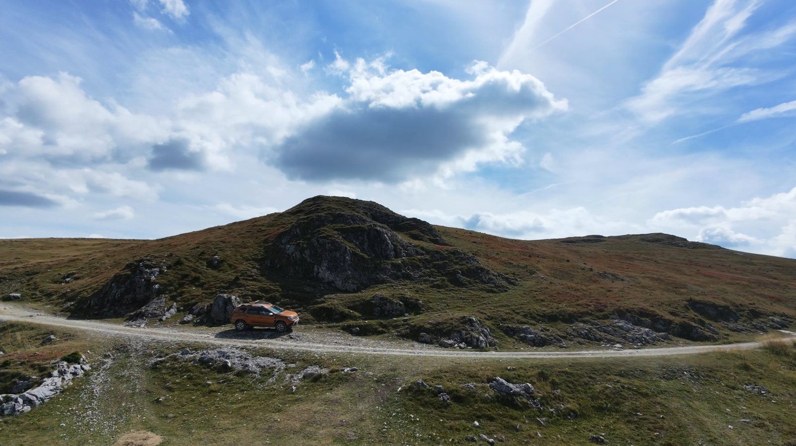 Our car on the Strategica ridge road below a rocky summit, under big summer clouds